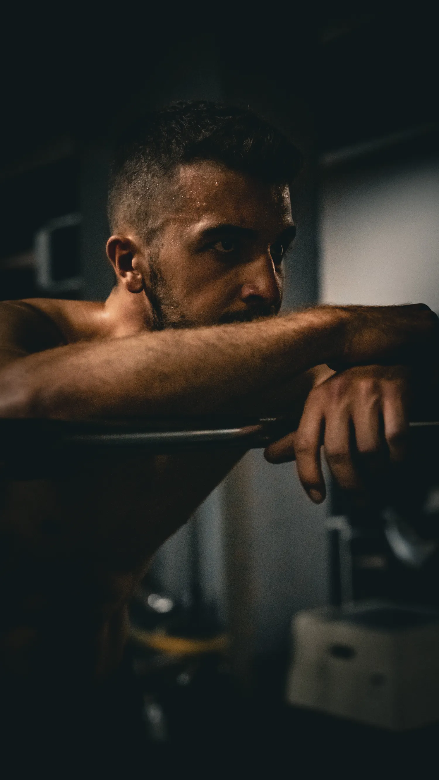 An athlete resting on a barbell in a dim gym