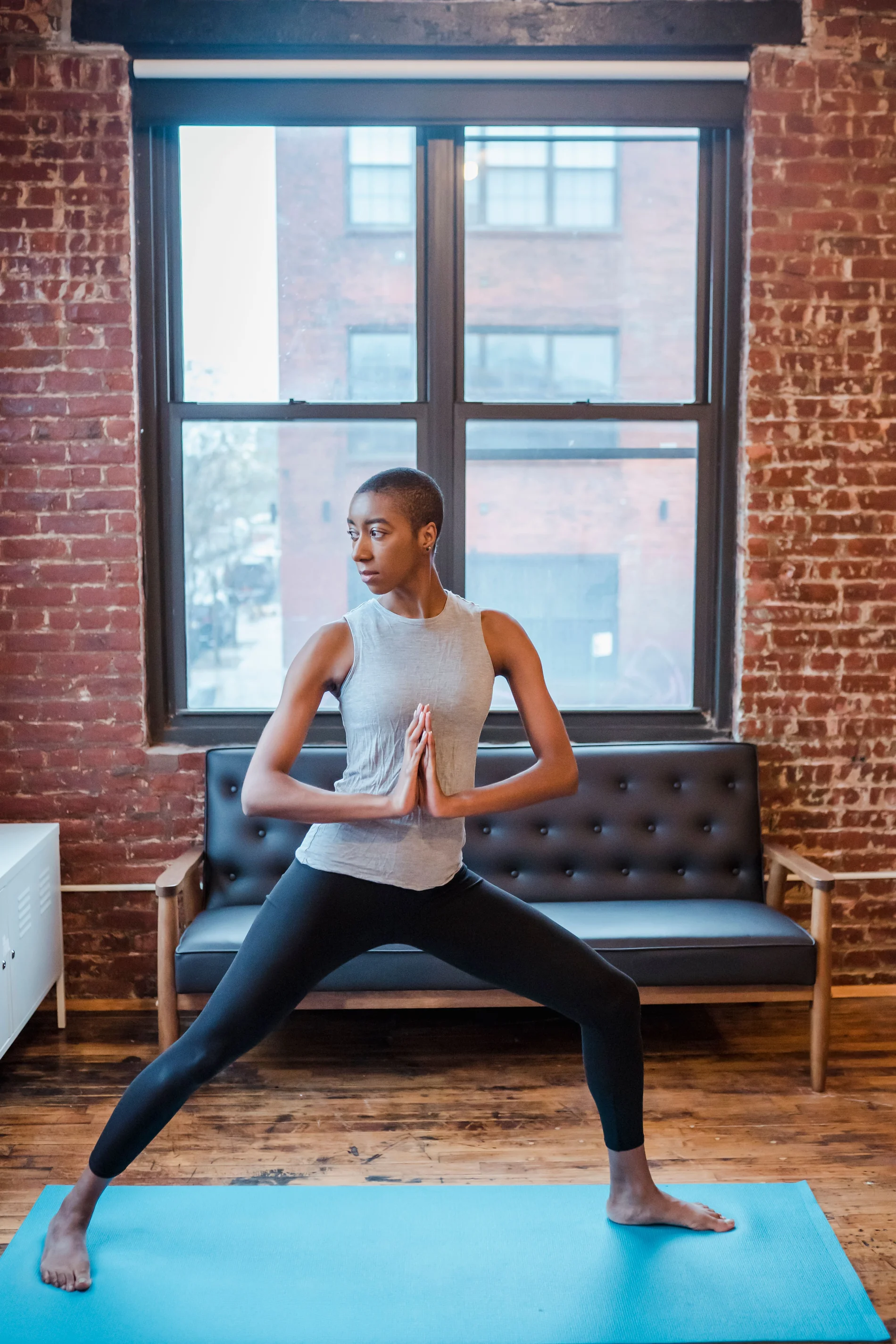 A woman in a crescent lunge, hands joined, in a sunlit loft